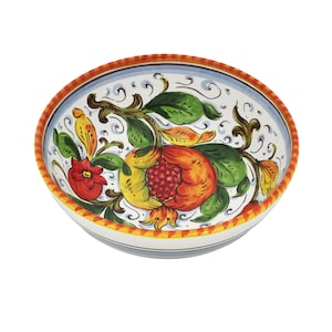 K&ouml;nnte beinhalten: Eine handbemalte Keramikschale mit einem Granatapfel-Design. Das Innere der Schale ist wei&szlig; und mit einer detaillierten Illustration eines Granatapfels, Bl&auml;ttern und Blumen in Rot-, Gelb- und Gr&uuml;nt&ouml;nen verziert. Der Rand ist mit orangefarbenen und blauen Streifen verziert.