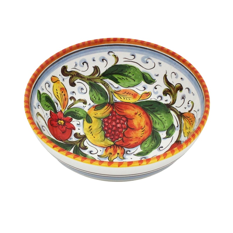 K&ouml;nnte beinhalten: Eine handbemalte Keramikschale mit einem Granatapfel-Design. Das Innere der Schale ist wei&szlig; und mit einer detaillierten Illustration eines Granatapfels, Bl&auml;ttern und Blumen in Rot-, Gelb- und Gr&uuml;nt&ouml;nen verziert. Der Rand ist mit orangefarbenen und blauen Streifen verziert.