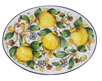 Puede incluir: Plato ovalado de cerámica con un diseño de limones pintados a mano. El plato blanco presenta limones amarillos, hojas verdes y vides marrones, con un borde azul. El diseño incluye pequeños acentos florales azules y rojos.