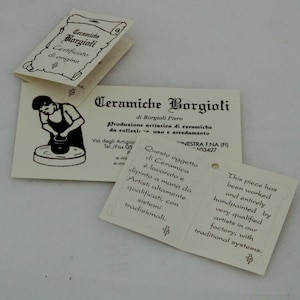 K&ouml;nnte beinhalten: Mehrere cremefarbene Papierschilder mit italienischem und englischem Text. Die Schilder zeigen die W&ouml;rter "Ceramiche Borgioli" und "Certificato di origine". Ein Schild zeigt einen T&ouml;pfer. Die Schilder beschreiben die Keramikherstellung.