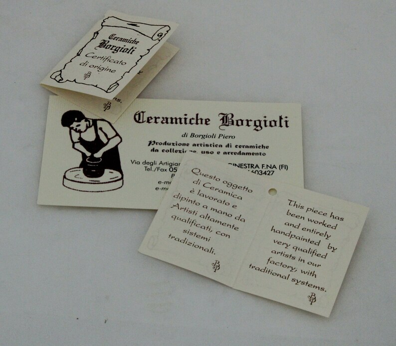 K&ouml;nnte beinhalten: Mehrere cremefarbene Papierschilder mit italienischem und englischem Text. Die Schilder zeigen die W&ouml;rter "Ceramiche Borgioli" und "Certificato di origine". Ein Schild zeigt einen T&ouml;pfer. Die Schilder beschreiben die Keramikherstellung.