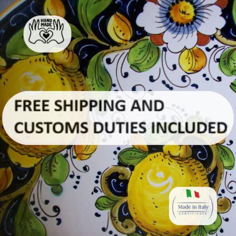 May include: A close-up of a ceramic plate with a hand-painted design. The plate features yellow lemons, green leaves, and white flowers with blue and black accents. The plate has a "Hand Made" sticker and a "Made in Italy" certificate.