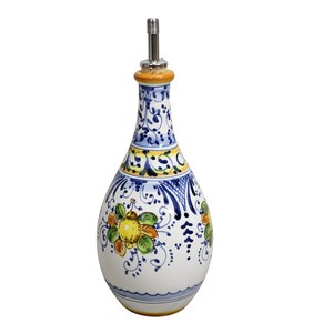 May include: A white ceramic olive oil bottle with a decorative floral design in blue, yellow, and orange. The bottle has a stainless steel spout and a painted design around the neck and body. The bottle is approximately 10 inches tall.