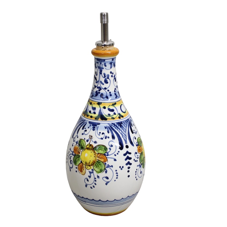 May include: A white ceramic olive oil bottle with a decorative floral design in blue, yellow, and orange. The bottle has a stainless steel spout and a painted design around the neck and body. The bottle is approximately 10 inches tall.