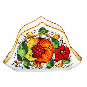 Può includere: Portatovaglioli in ceramica bianca con un design dipinto a mano raffigurante un melograno, un fiore rosso e foglie verdi. I bordi sono rifiniti con accenti gialli e blu, creando un pezzo vibrante e decorativo.