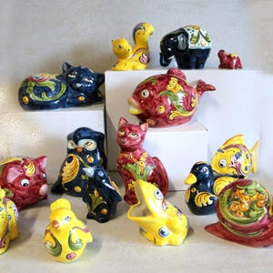 May include: A collection of colorful ceramic animal figurines, including a cat, owl, fish, duck, snail, and elephant. The figurines are hand-painted with intricate floral and geometric designs in shades of red, blue, yellow, and green.