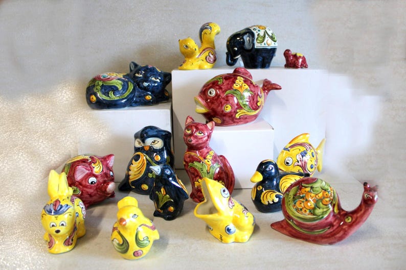 May include: A collection of colorful ceramic animal figurines, including a cat, owl, fish, duck, snail, and elephant. The figurines are hand-painted with intricate floral and geometric designs in shades of red, blue, yellow, and green.