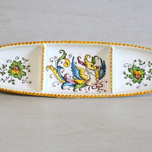 Peut inclure: Un plat de service en céramique blanche avec trois sections. La section centrale présente un motif peint coloré d'un oiseau avec un motif floral. Les deux sections latérales ont un simple motif floral.