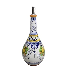 May include: A white ceramic olive oil bottle with a decorative design. The bottle features a long neck and a bulbous body, adorned with blue, yellow, and green floral patterns. The word "OLIO" is visible on the bottle. A metal spout is at the top.