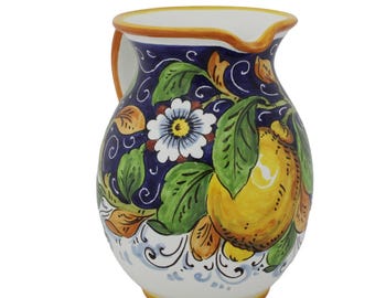 Puede incluir: Jarra de cerámica con asa, con un diseño vibrante de limones, hojas y flores. La jarra tiene una base blanca, un fondo azul y un borde amarillo. Los detalles pintados a mano incluyen acentos naranjas y verdes.