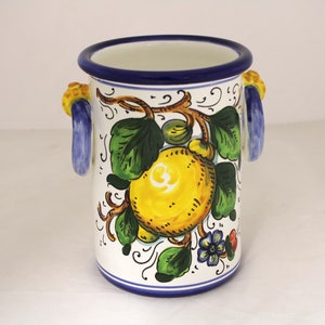 Può includere: Portautensili in ceramica bianca con bordo blu e un motivo a limone. Il portautensili ha due manici blu e presenta un limone giallo con foglie verdi e un piccolo fiore blu.
