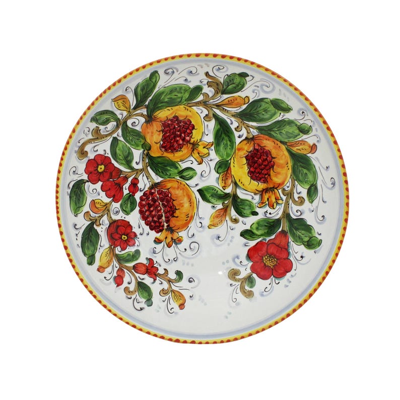 May include: A white ceramic decorative plate with a hand-painted design of pomegranates and flowers. The pomegranates are yellow and red, with green leaves and red flowers. The rim has a yellow and blue border.