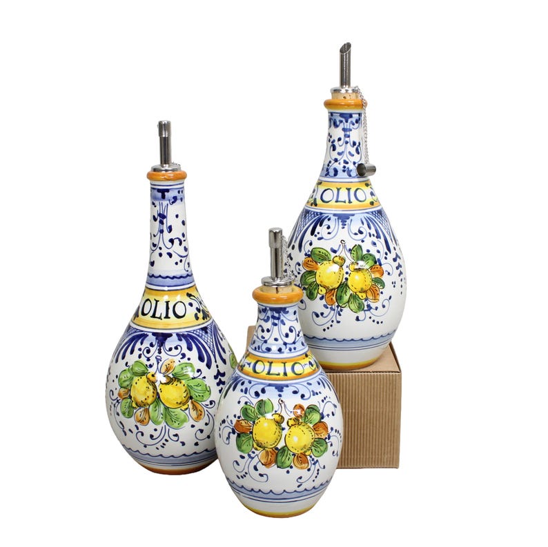 May include: Three ceramic olive oil bottles with stainless steel spouts. The bottles are white with blue and yellow floral designs and the word "OLIO". The bottles are of varying sizes.
