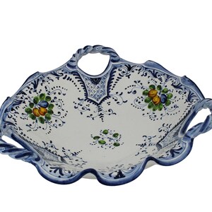 K&ouml;nnte beinhalten: Wei&szlig;es Keramik-Serviertablett mit blauen Verzierungen und Griffen. Das Tablett hat ein Blumendesign mit gr&uuml;nen, gelben und blauen Akzenten. Die Griffe haben ein gedrehtes Seil-Design.
