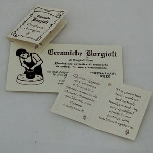 Puede incluir: Etiquetas de papel blanquecino con texto en italiano e ingl&eacute;s. Las etiquetas presentan las palabras "Ceramiche Borgioli" e incluyen ilustraciones de cer&aacute;mica en proceso de elaboraci&oacute;n. Las etiquetas describen las piezas de cer&aacute;mica como pintadas a mano.