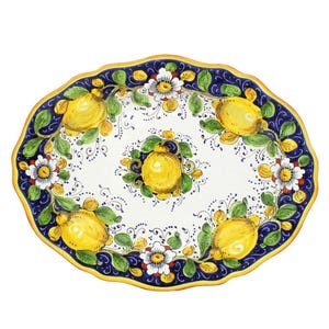 May include: Oval ceramic serving platter with a scalloped edge. The white surface is decorated with yellow lemons, green leaves, and white flowers against a blue border with a yellow trim. A decorative piece for serving.
