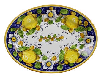 May include: Oval ceramic serving platter with a hand-painted design. The platter features a white center with yellow lemons, green leaves, and white flowers. The rim is blue with a yellow border. A decorative piece for serving food.