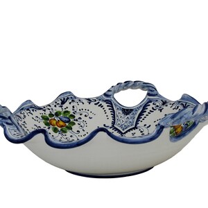 K&ouml;nnte beinhalten: Wei&szlig;e Keramik-Serviersch&uuml;ssel mit gewelltem Rand und geflochtenem Griff. Die Sch&uuml;ssel ist mit blau-wei&szlig;en Blumenmustern und Akzenten verziert. Der Rand ist mit einem dunkelblauen Rand versehen.