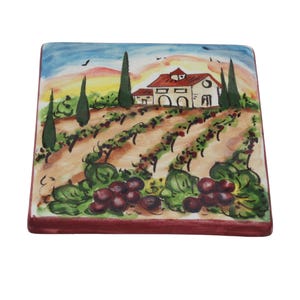 May include: Square ceramic tile featuring a hand-painted vineyard scene. The artwork depicts a farmhouse with a red roof, rows of grapevines, and a sunset sky. The tile's edges are a deep red, and the overall design is colorful and detailed.