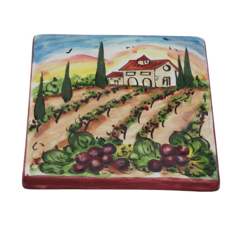 May include: Square ceramic tile featuring a hand-painted vineyard scene. The artwork depicts a farmhouse with a red roof, rows of grapevines, and a sunset sky. The tile's edges are a deep red, and the overall design is colorful and detailed.