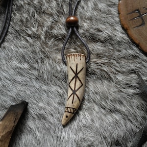 May include: A brown leather cord necklace with a wooden bead and a carved bone pendant. The pendant is shaped like a tooth and has a geometric design etched into it.