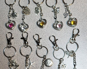 May include: Twelve silver keychains with a variety of charms and colorful heart-shaped crystals. Each keychain has a silver ring and a silver clip.