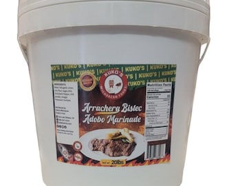 Puede incluir: Un cubo de plástico blanco con una etiqueta roja y blanca. La etiqueta dice "Kuko's Michoacan Foods" y "Arrachera Bistec Adobo Marinade". El cubo contiene 20 libras de adobo.
