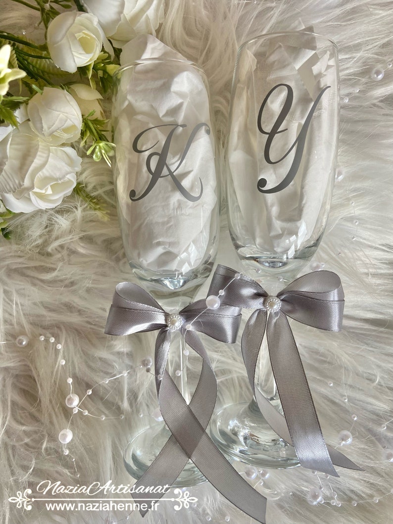 May include: Two champagne flutes with gray satin bows and pearl accents. The flutes are personalized with the letters "K" and "Y" in a cursive font.