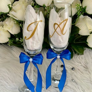 May include: Two champagne flutes with blue satin bows and gold letter decals. The letters are "J" and "A".