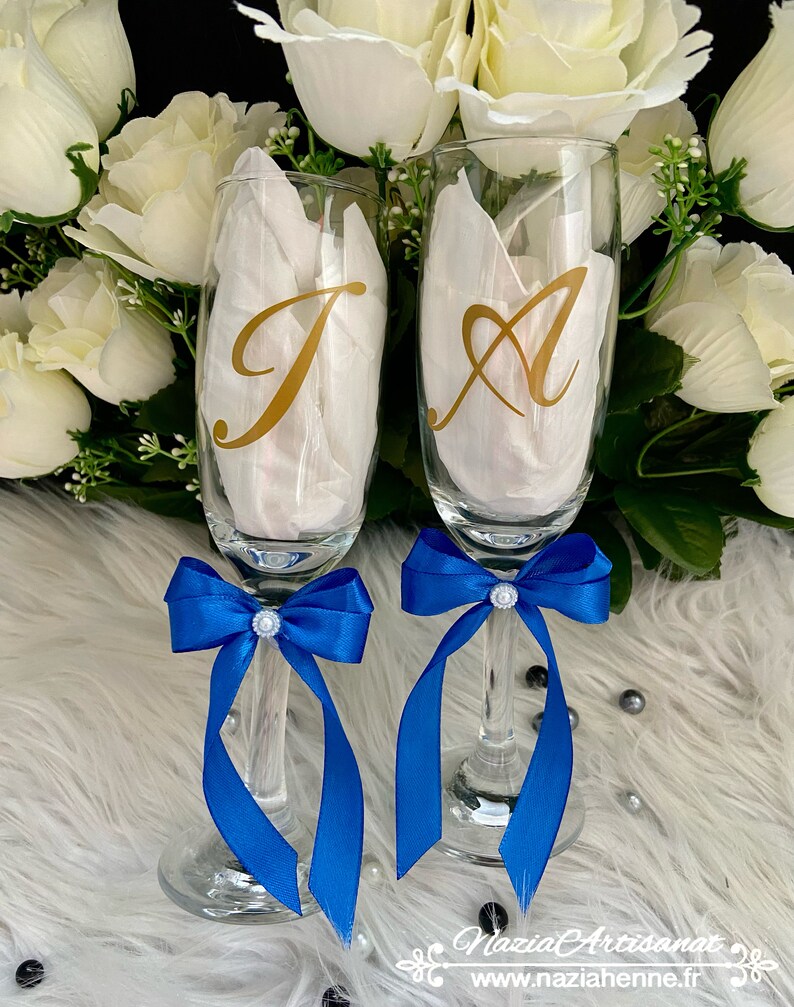 May include: Two champagne flutes with blue satin bows and gold letter decals. The letters are "J" and "A".
