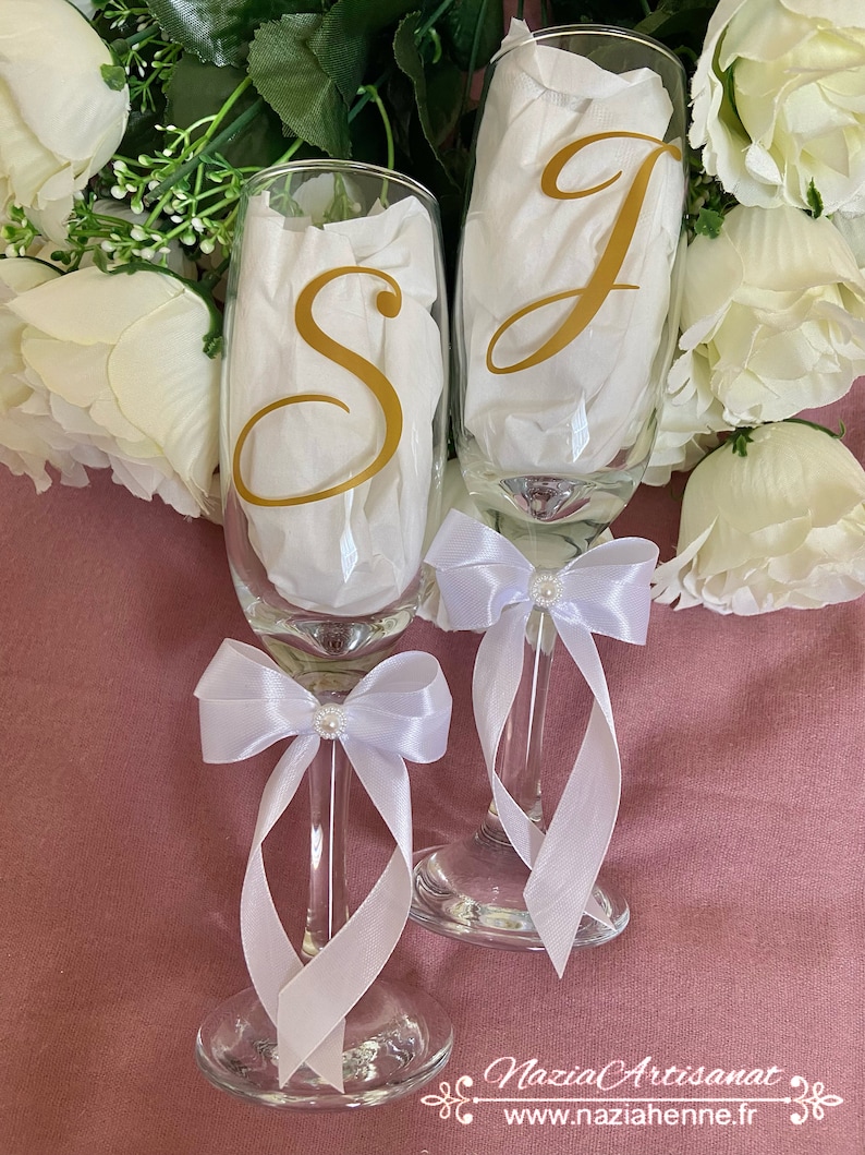 May include: Two champagne flutes with white satin bows and pearl accents. The flutes are decorated with gold vinyl letters, "S" and "J".