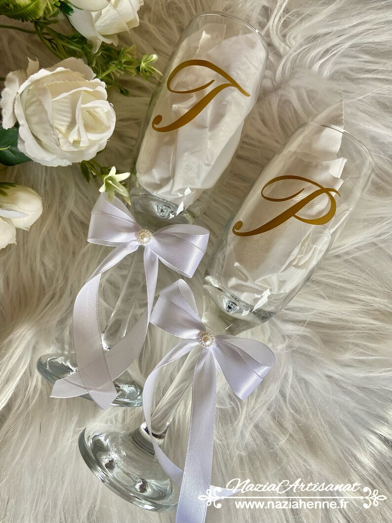May include: Two champagne flutes with white satin ribbons and pearl accents. The flutes are decorated with gold vinyl letters, one with the letter "J" and the other with the letter "P".