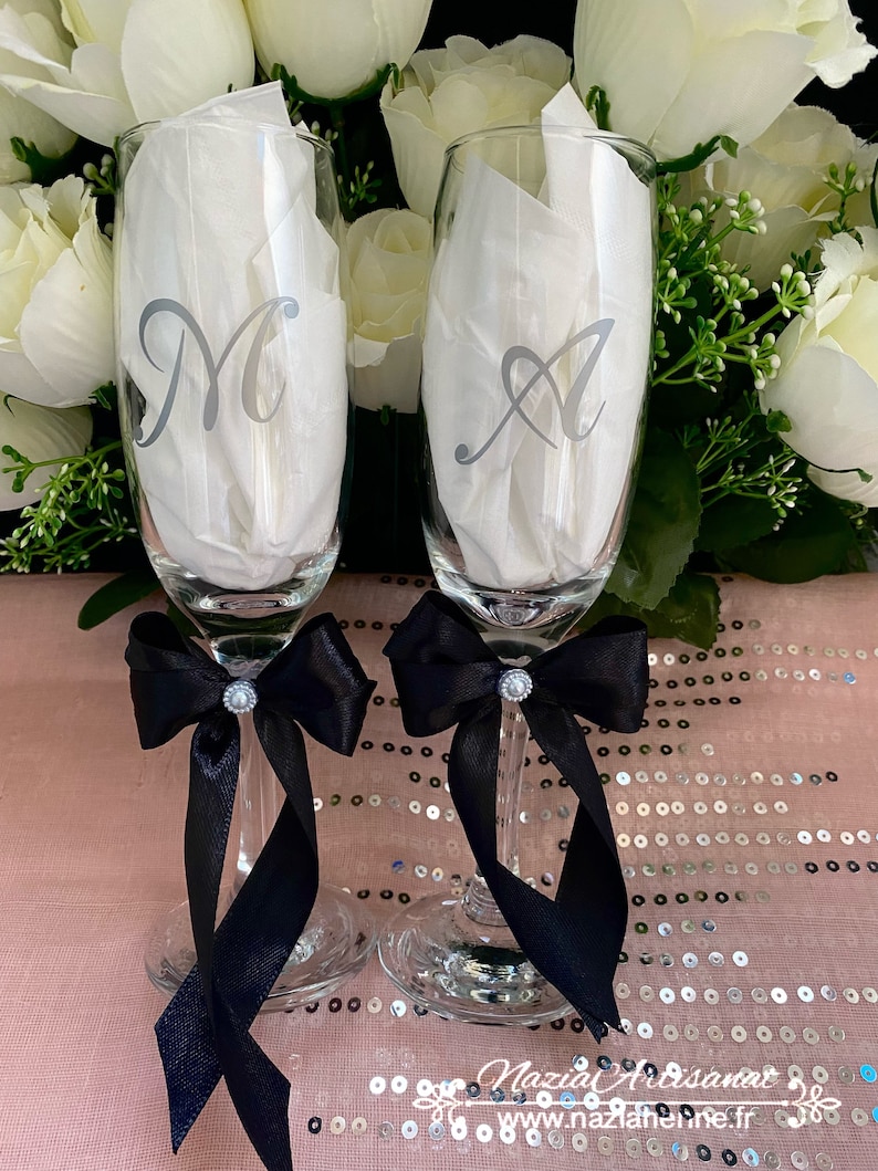 May include: Two champagne flutes with black satin bows and rhinestones. The flutes are personalized with the letters "M" and "A" in silver.