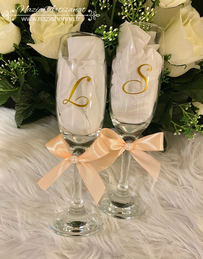 May include: Two champagne flutes with peach-colored bows and gold lettering. The flutes are decorated with the letters "L" and "S".