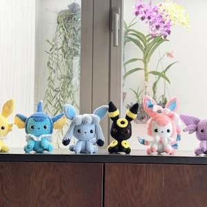 May include: A set of six small, handmade crochet plush toys featuring various creatures with distinct color schemes including yellow, blue, light blue, black with yellow rings, pink with white accents, and light purple with a red forehead gem.