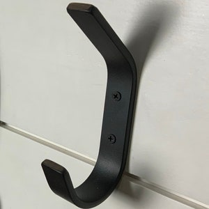 May include: Two black metal hooks mounted on a white wall. A brown leather strap with silver accents hangs from one of the hooks.