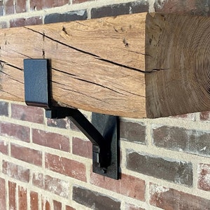 May include: A rustic wooden mantel shelf with black metal brackets. The shelf is mounted on a brick wall.