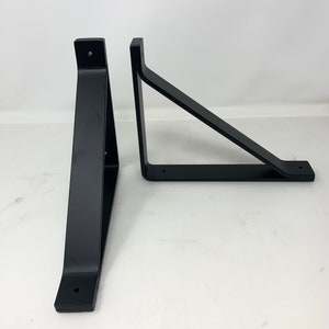 May include: Two black metal shelf brackets, each with a triangular shape and two holes for mounting.