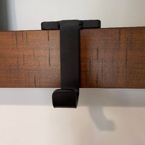 May include: Black metal hook for hanging items on a wooden shelf.