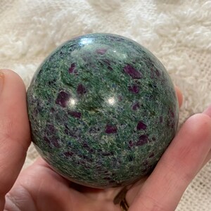 May include: A green and purple sphere with a speckled pattern. The sphere is made of a polished stone.