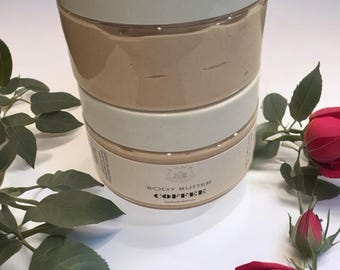 Może przedstawiać: Trzy słoiki masła do ciała, ułożone jeden na drugim. Górny słoik jest oznaczony etykietą "Body Butter", a dolny słoik etykietą "Body Butter Coffee". Słoiki znajdują się na białym tle z zielonymi liśćmi i czerwonymi różami.