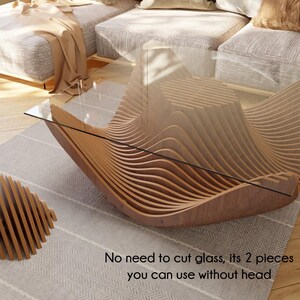 May include: A modern coffee table with a unique wave-like design, constructed from layered wooden slats. The table features a clear glass top and a matching wooden accent piece. The text on the image says, "No need to cut glass, its 2 pieces you can use without head."