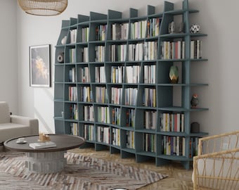 May include: A blue, modern, modular bookshelf with a wavy design. The bookshelf is filled with books and decorative objects. The bookshelf is in a living room setting with a rug, coffee table, and chair.