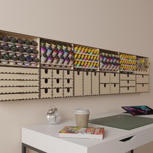 May include: A wall-mounted wooden storage unit with multiple drawers and shelves for organizing small items. The unit is made of light brown wood and has a modern design. It is filled with rows of small paint bottles in various colors.
