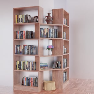 K&ouml;nnte beinhalten: Ein Eckregal aus Holz mit mehreren Regalbrettern, die mit B&uuml;chern gef&uuml;llt sind. Das Regal hat eine helle Holzoptik und ist mit einer Blumenvase und einem Korb dekoriert.