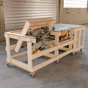 May include: A light-colored wooden workbench on casters featuring an integrated miter saw mounted on a flip-top mechanism and a table saw embedded into the flat surface. The structure is constructed from light wood beams with a modular design.