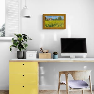 May include: A framed painting of a yellow field with a small house in the distance. The painting is hanging on a white wall above a desk with a computer, a chair, and a yellow drawer unit.