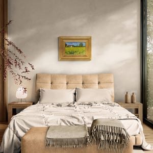 May include: A bedroom interior with a bed, a nightstand, and a framed landscape painting on the wall. The bed has a white duvet and two pillows. The nightstand has a lamp and a vase with flowers. The painting depicts a field of yellow flowers with a house in the background.
