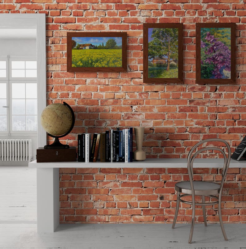 May include: A white shelf with a globe, books, and a wooden vase sits in front of a red brick wall. Three framed pictures hang on the wall above the shelf. A chair sits to the right of the shelf.