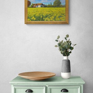 May include: A framed painting of a yellow field with a white farmhouse in the distance. The painting is hanging on a white wall above a light green dresser with six drawers.